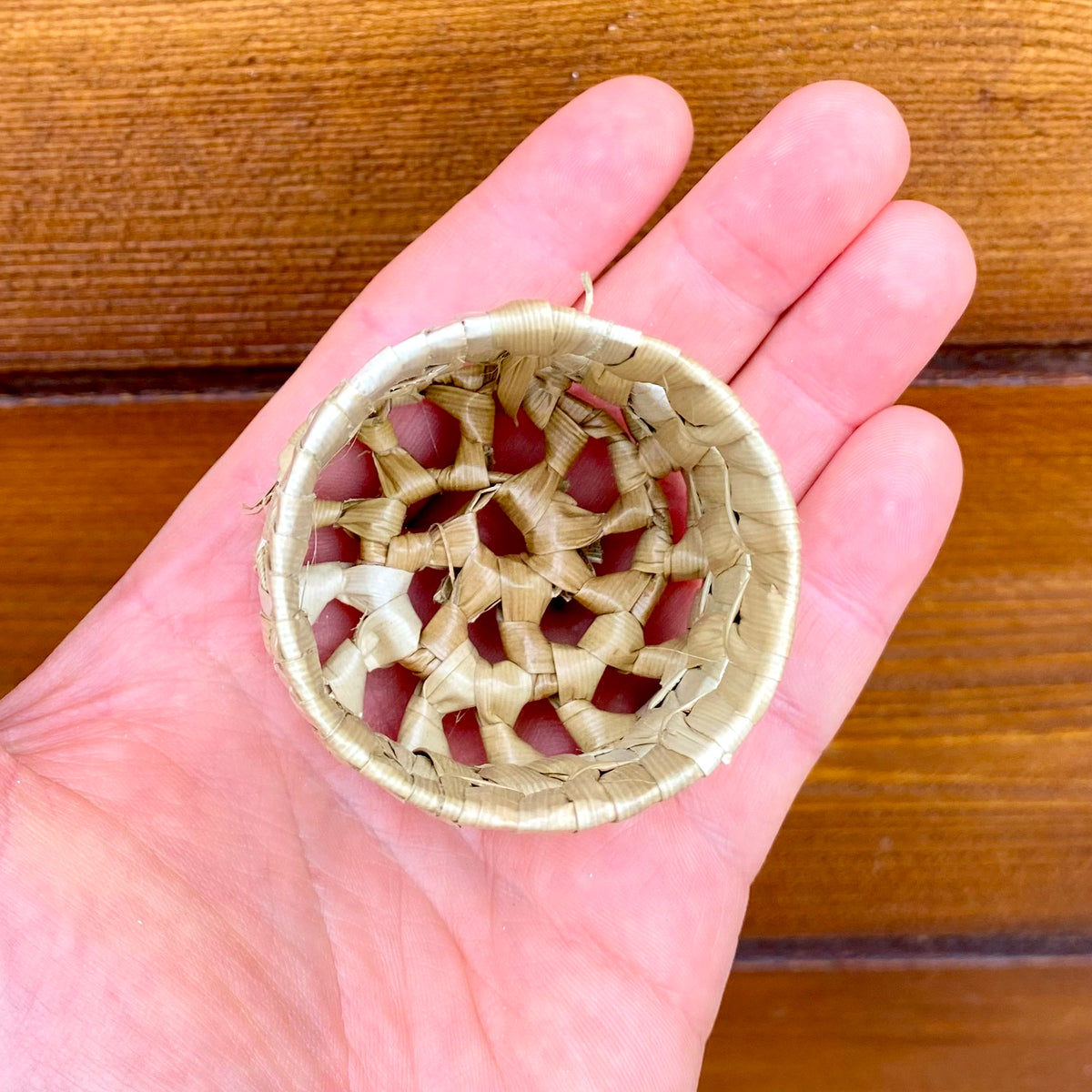 Hand holding a mini woven pot against a wooden background