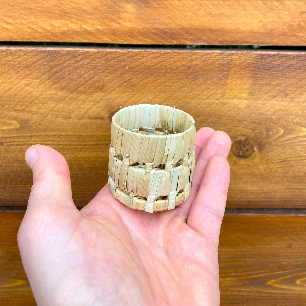 Hand holding a mini woven pot against a wooden background